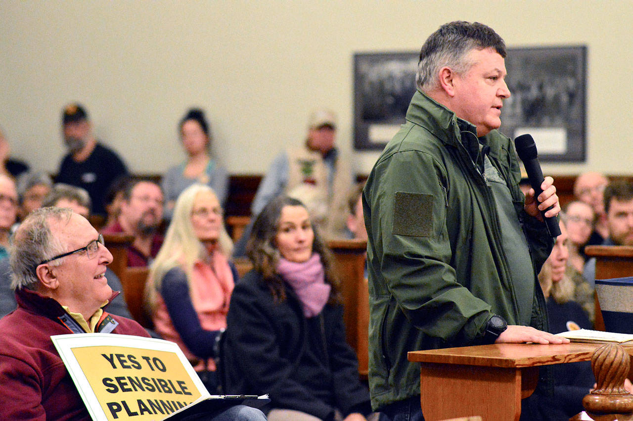 Fort Discovery operator Joe D’Amico, standing, speaks to the Jefferson County commissioners about the moratorium that has put his proposed Tarboo Lake shooting range on hold. Peter Newland, left, a member of the Tarboo Ridge Coalition who spoke against the new range, listens. (Diane Urbani de la Paz/for Peninsula Daily News)