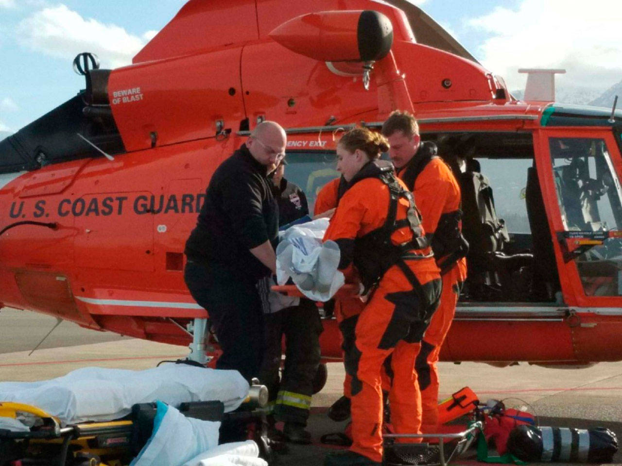 Members of a MH-65 Dolphin helicopter crew from Coast Guard Air Station/Sector Field Officer Port Angeles and emergency medical service personnel move an injured hiker to a stretcher on the air field at the air station Saturday. (Eric Mangiarelli, petty officer 3rd class/U.S. Coast Guard)