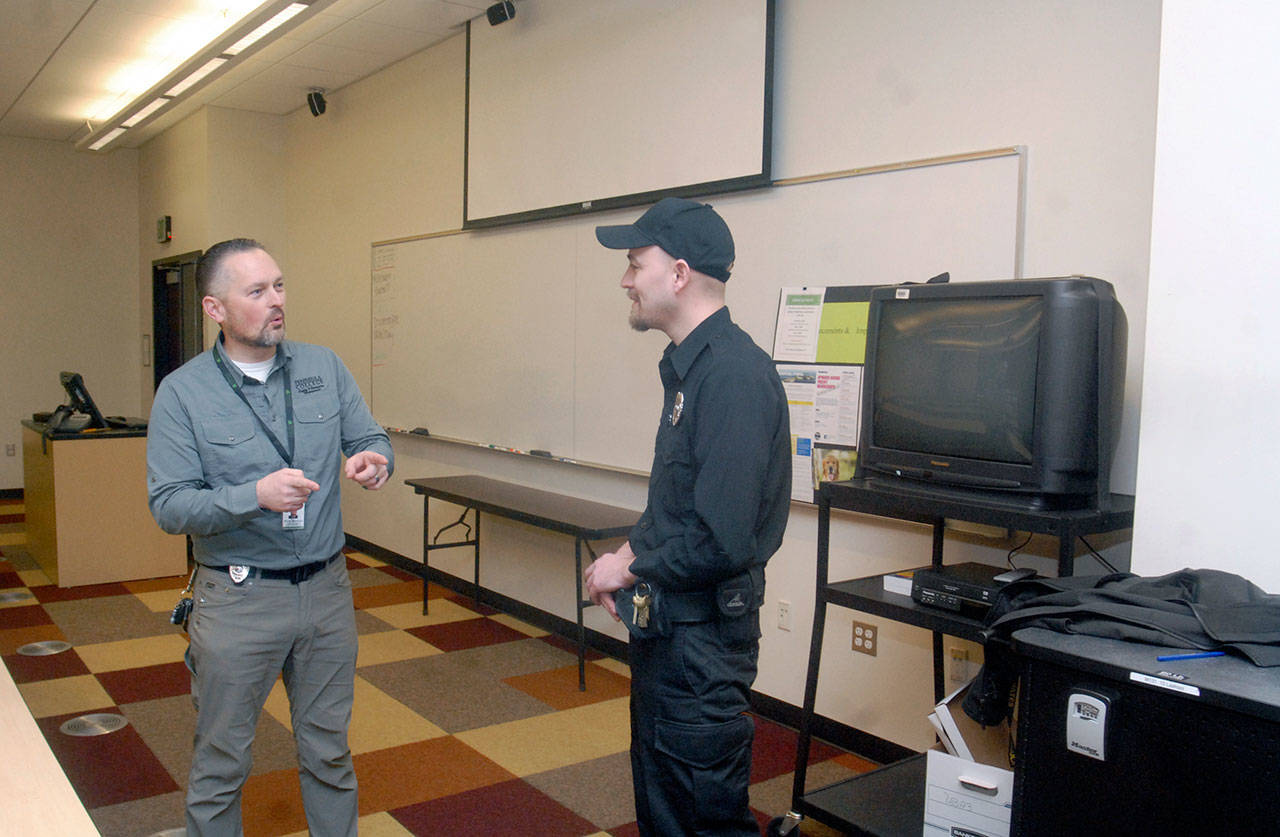 Marty Martinez, campus safety operations manager for Peninsula College, left, and campus safety officer Alec Risk discuss active shooter drills in a classroom in Keegan Hall on Friday in Port Angeles. In an active shooter situation, students would huddle against the wall at the front of the class, out of sight of anyone looking in from the outside hallway. (Keith Thorpe/Peninsula Daily News)
