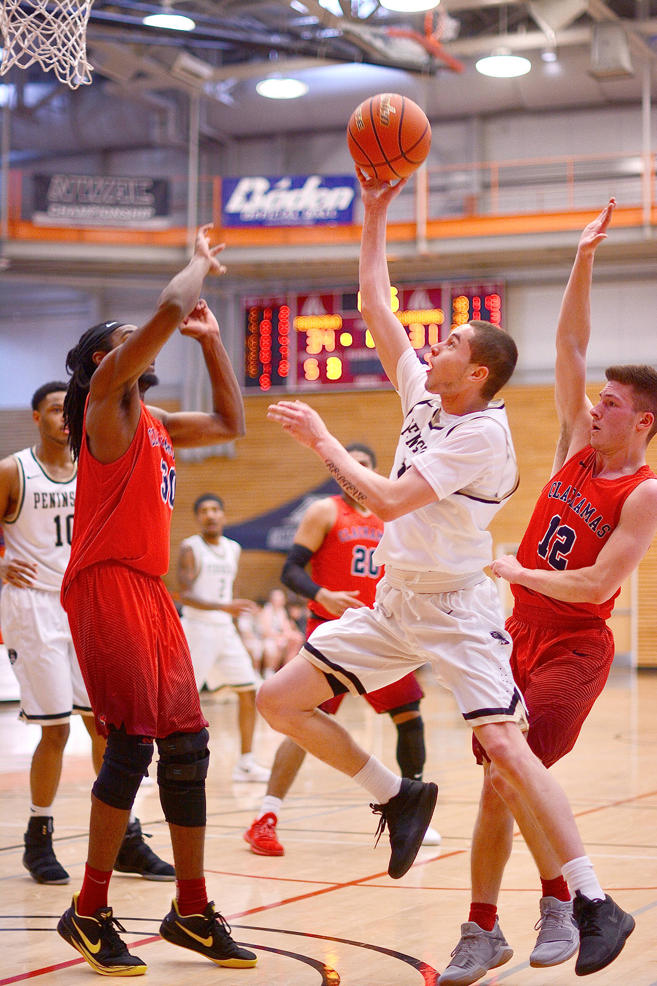 Jay Cline Peninsula’s James Buckley, center, eyes the rim as Clackamas’ Isaiah Gentry, left, and Briggs Young defend during the Pirates win Saturday at the NWAC Men’s Basketball Championships at Everett Community College.