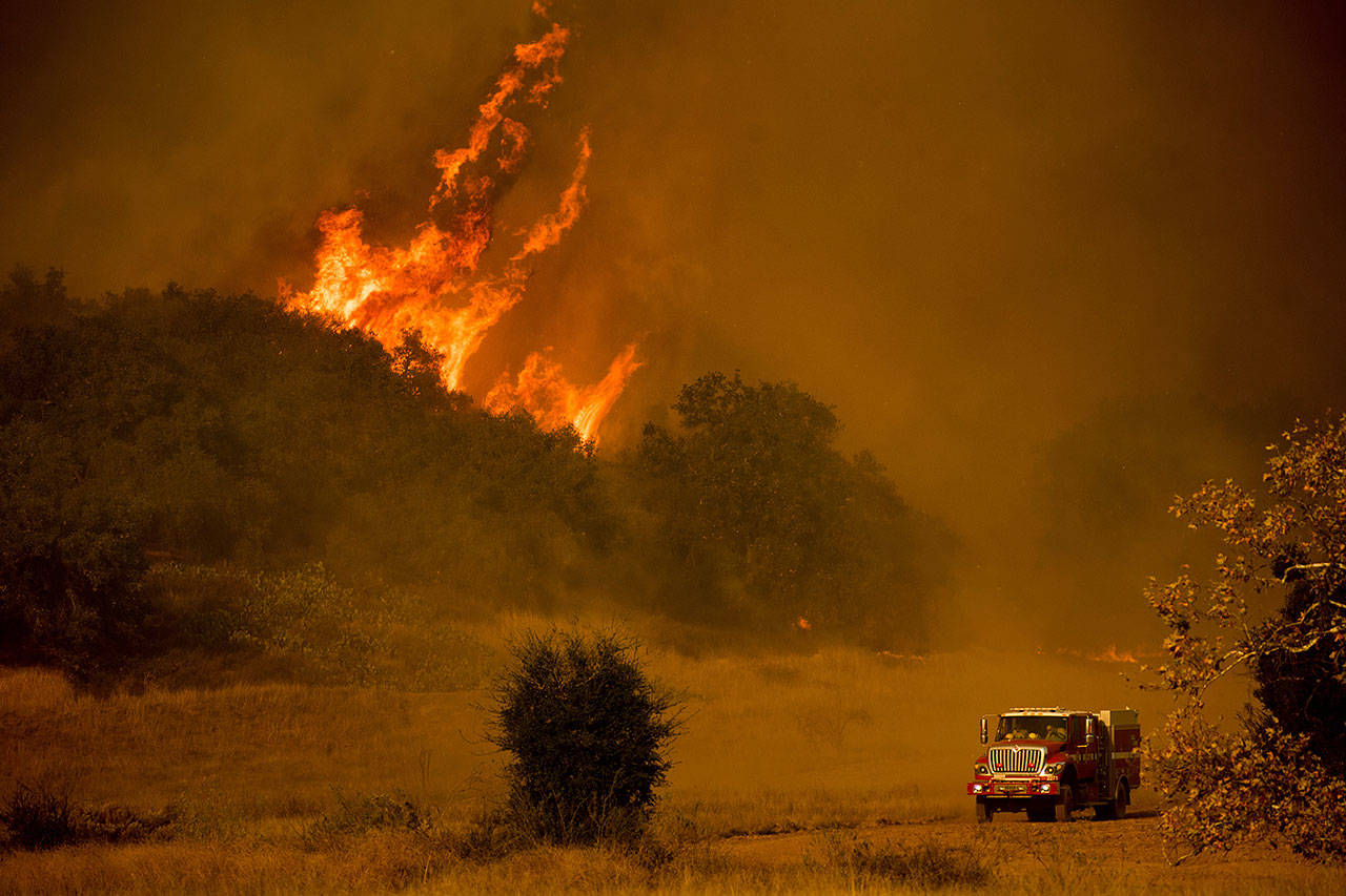 In this Dec. 9, 2017, file photo a fire engine passes flames as a wildfire burns along Santa Ana Road near Ventura, Calif. (The Associated Press)