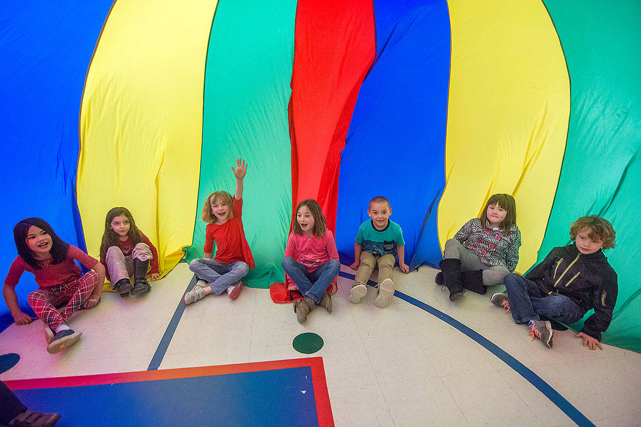 First-grade students at Hamilton Elementary School sit on the inside of a parachute during their physical education class, using captured air to make a “tent” Wednesday. (Jesse Major/Peninsula Daily News)