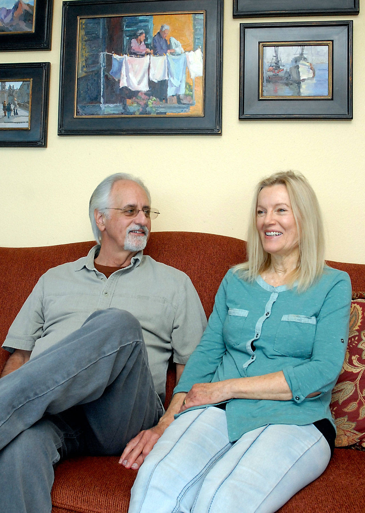 Against a backdrop of some of her own paintings, Jeanne Edwards, along with her husband, Mike Edwards, talks about how some of her works ended up in a church in Kenya as a “thank you” to the donor who provided the organ for her husband’s heart transplant. (Keith Thorpe/Peninsula Daily News)