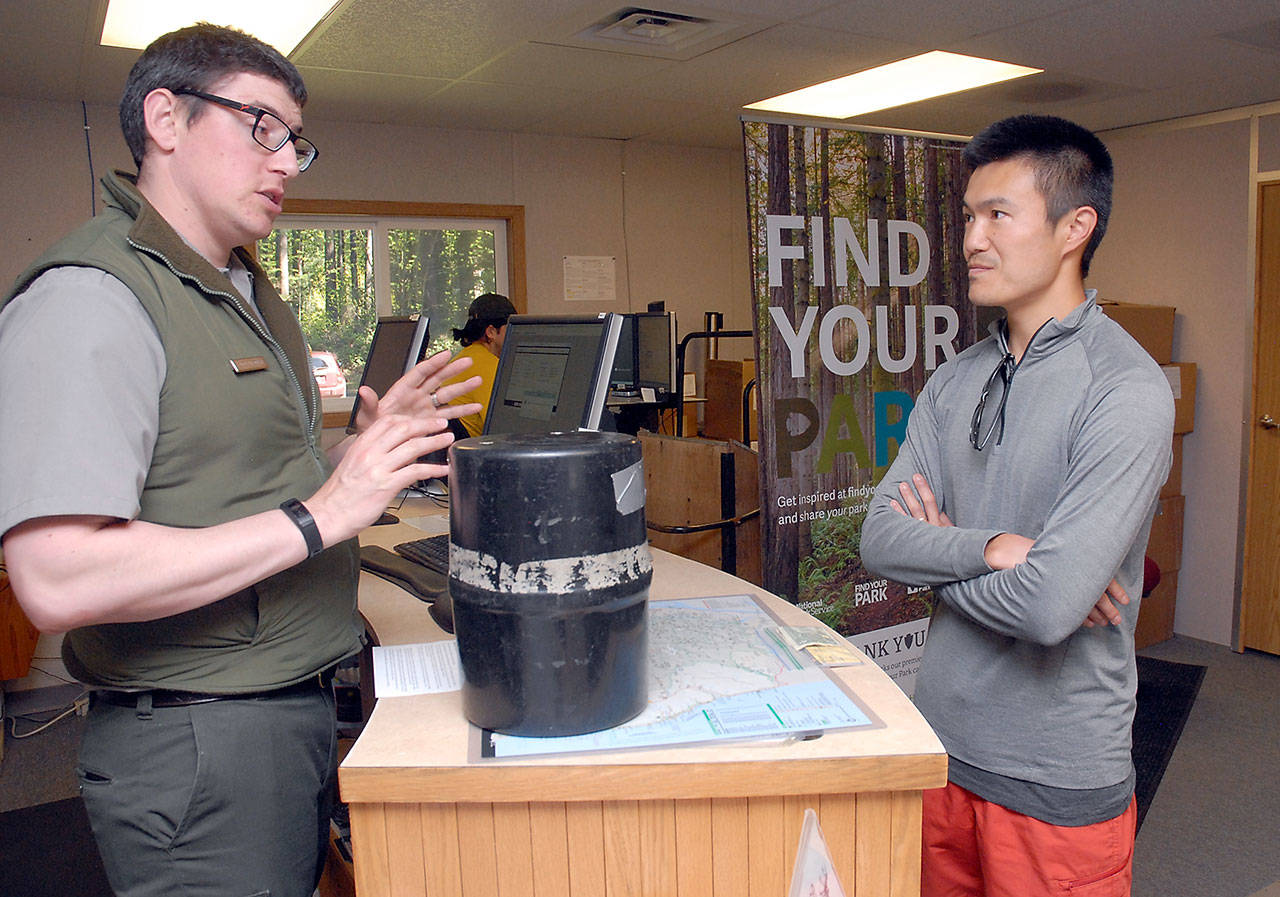 Wilderness ranger Jed Friedman, left, explains the proper use of a bear can to Yuji Murai of Seattle at the temporary Olympic National Park Wilderness Center in Port Angeles on Saturday. (Keith Thorpe/Peninsula Daily News)