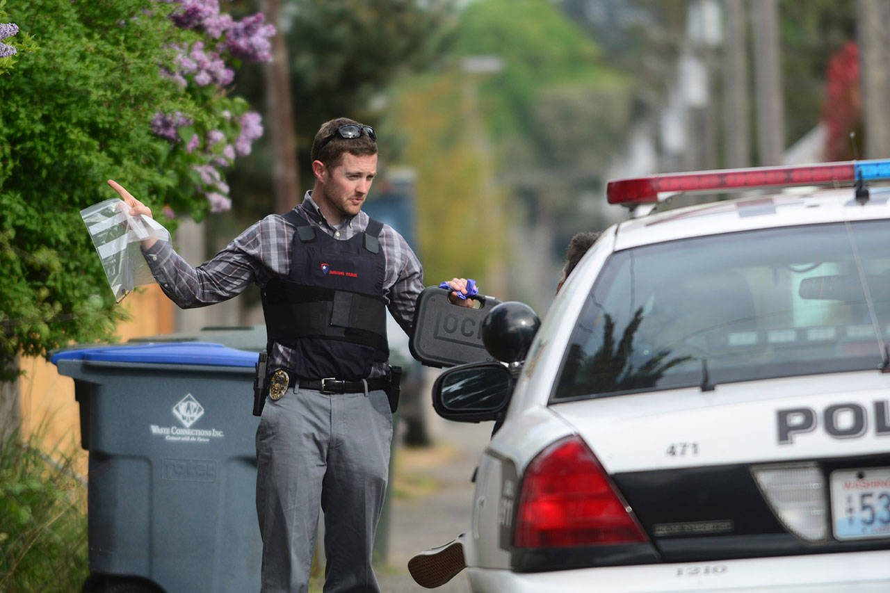 Port Angeles Police Department Detective Shane Martin, holding a bag containing spent casings and a container with a .40 caliber Glock handgun, talks to a man suspected of shooting a neighbor’s vehicle Tuesday afternoon. (Jesse Major/Peninsula Daily News)
