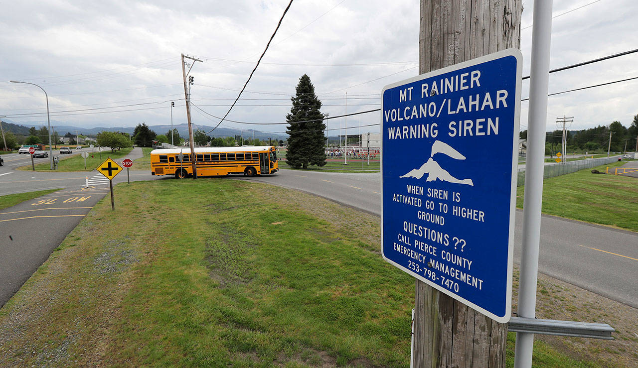 In this May 8 photo, a sign under a lahar warning siren is shown as a school bus drives near Orting Middle School in Orting. (Ted S. Warren/The Associated Press)