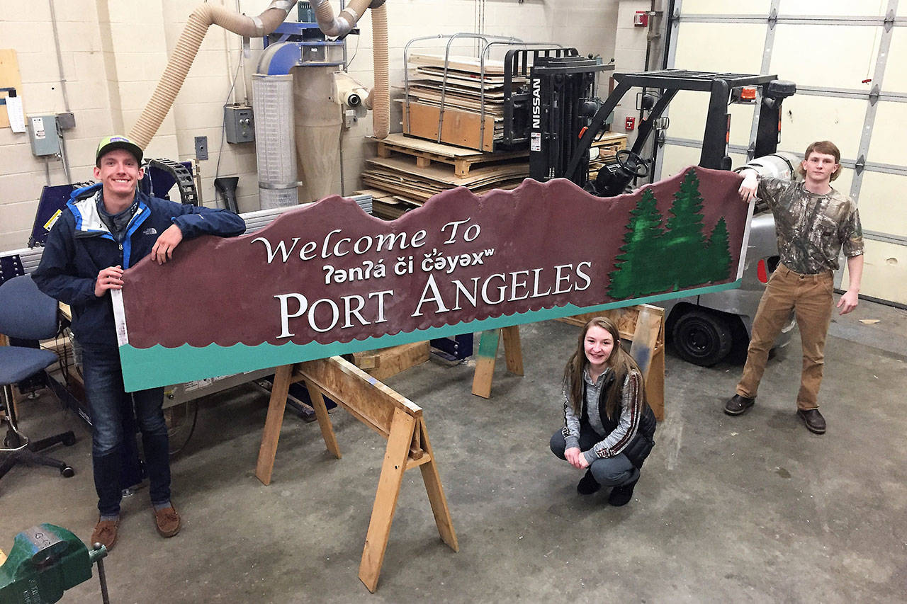 Port Angeles High School woodworking students Sawyer Larsen, left, Mariah Fortman and Glenn Deckart, right, with the sign they’ve been working on since September. The sign, with a fresh paint job, will be unveiled today. (Tim Branham/Port Angeles High School)