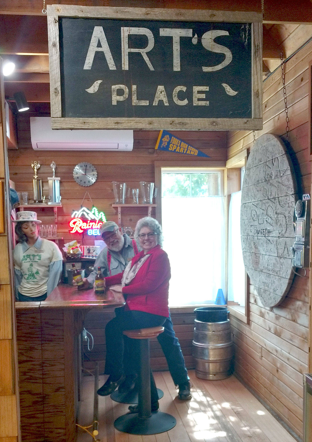 In the Forks Timber Museum, Joe and Linda Offutt sit in a reconstructed scene from Art’s Tavern, a historical hangout for thirsty folks in days past. (Zorina Barker/for Peninsula Daily News)