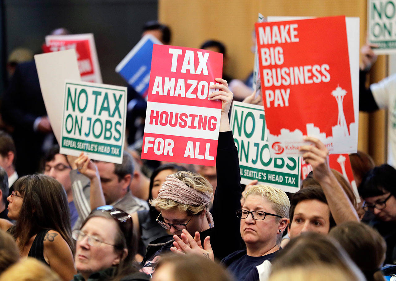 People attending a Seattle City Council meeting hold signs that read “Tax Amazon, Housing for All,” and “No Tax on Jobs” listen to public comment on the debate over a possible council vote whether or not to repeal a tax on large companies such as Amazon and Starbucks that was intended to combat a growing homelessness crisis Tuesday at City Hall in Seattle. (Ted S. Warren/The Associated Press)