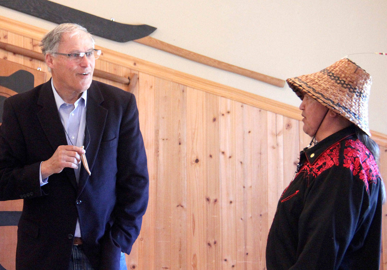 Gov. Jay Inslee, left, received gifts from the Quileute Tribe that included baskets and smoked smelt from Vince Penn, right, during his visit to La Push. Inslee here holds a small canoe carved by a young girl. (Christi Baron/Olympic Peninsula News Group)