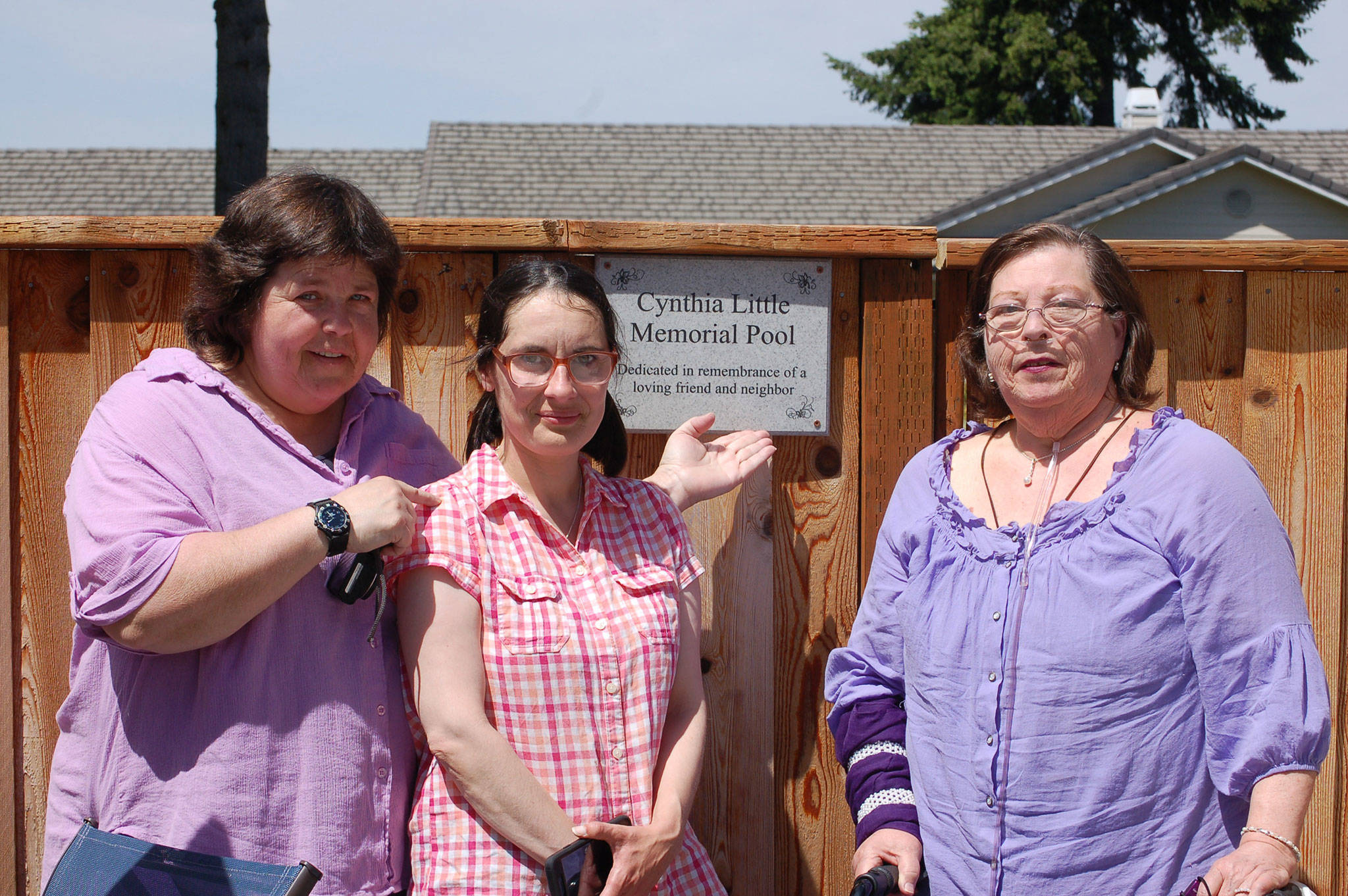 Bernie Philbin, left, CASA volunteer Emma Jones and Maggie Philbin, all close friends of Cynthia Little, stand next to Little’s dedication plaque at the Sunland Golf Country Club pool. (Erin Hawkins/Olympic Peninsula News Group)