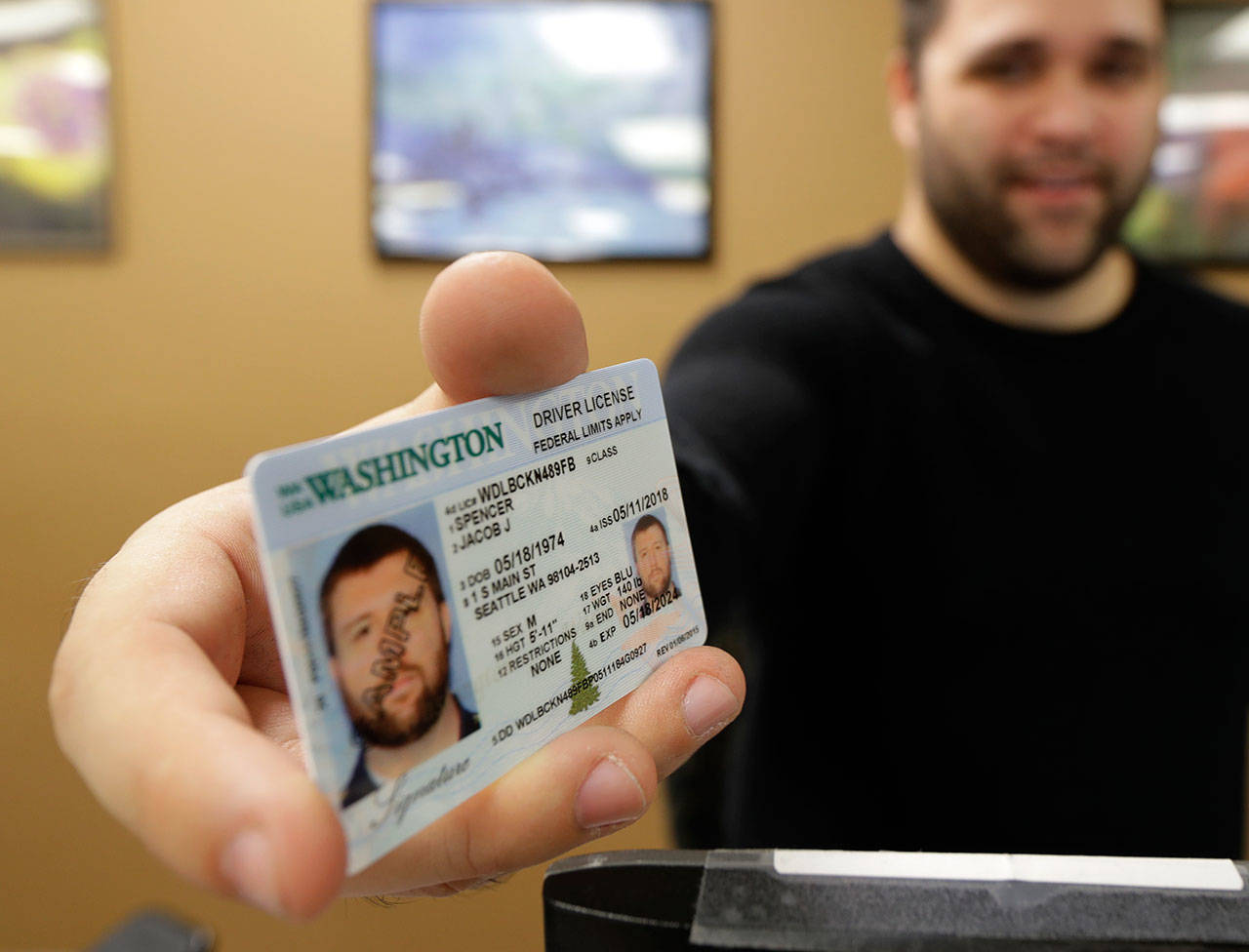 Ryan Norris, a license service representative at the state Deptartment of Licensing office in Lacey poses for a photo June 22 while holding a sample copy of a Washington drivers license. (Ted S. Warren/The Associated Press)