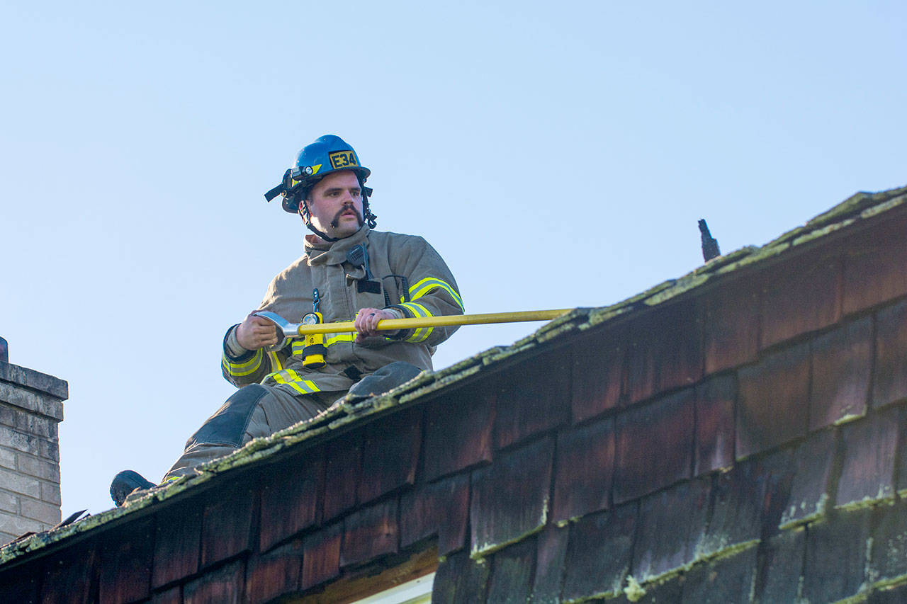 Clallam County Fire District No. 3 Firefighter Bryce Miginley overhauls a section of roof that caught fire near Sequim on Sunday. (Jesse Major/Peninsula Daily News)