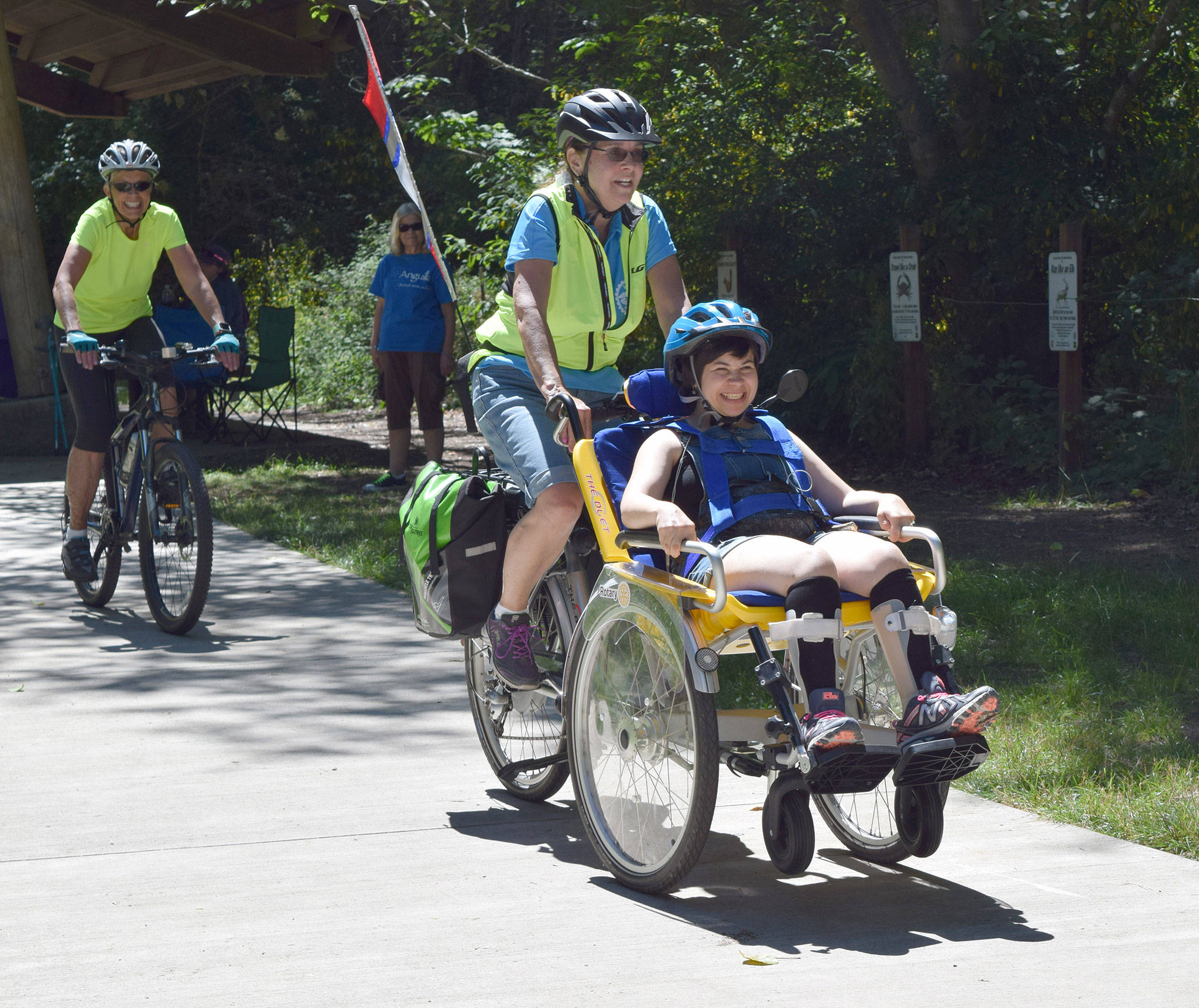 Piloted by Sequim Wheelers volunteer Elaine Cates, center, Kaitlyn Winn, foreground, enjoyed a ride on a duet wheelchair bicycle during a Clallam Mosaic sponsored field trip to Railroad Bridge Park on July 13. Riding as a safety was Sequim Wheelers volunteer Michele Fraker.