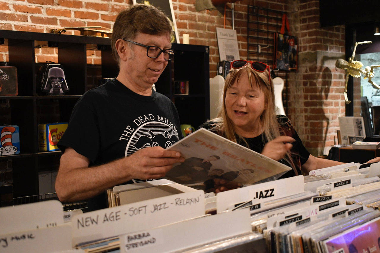 Mark Hering and Marie Campanoli check out a classic Beatles album in their store, Quimper Sound in Port Townsend’s Undertown. They are selling the store which comes with collectibles and 50,000 vinyl albums. A true audiophile, Hering said music has always played a part in his life. (Jeannie McMacken/Peninsula Daily News)