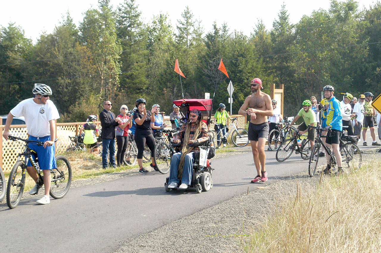 Ian Mackay and his supporters stop to celebrate after crossing the Clallam-Jefferson County line on the Olympic Discovery Trail at Diamond Point Road on Friday. Mackay had traveled on his wheelchair from Coeur d’Alene, Idaho to highlight the need for wheelchair-accessible trails in Washington. (Rob Ollikainen/Peninsula Daily News)