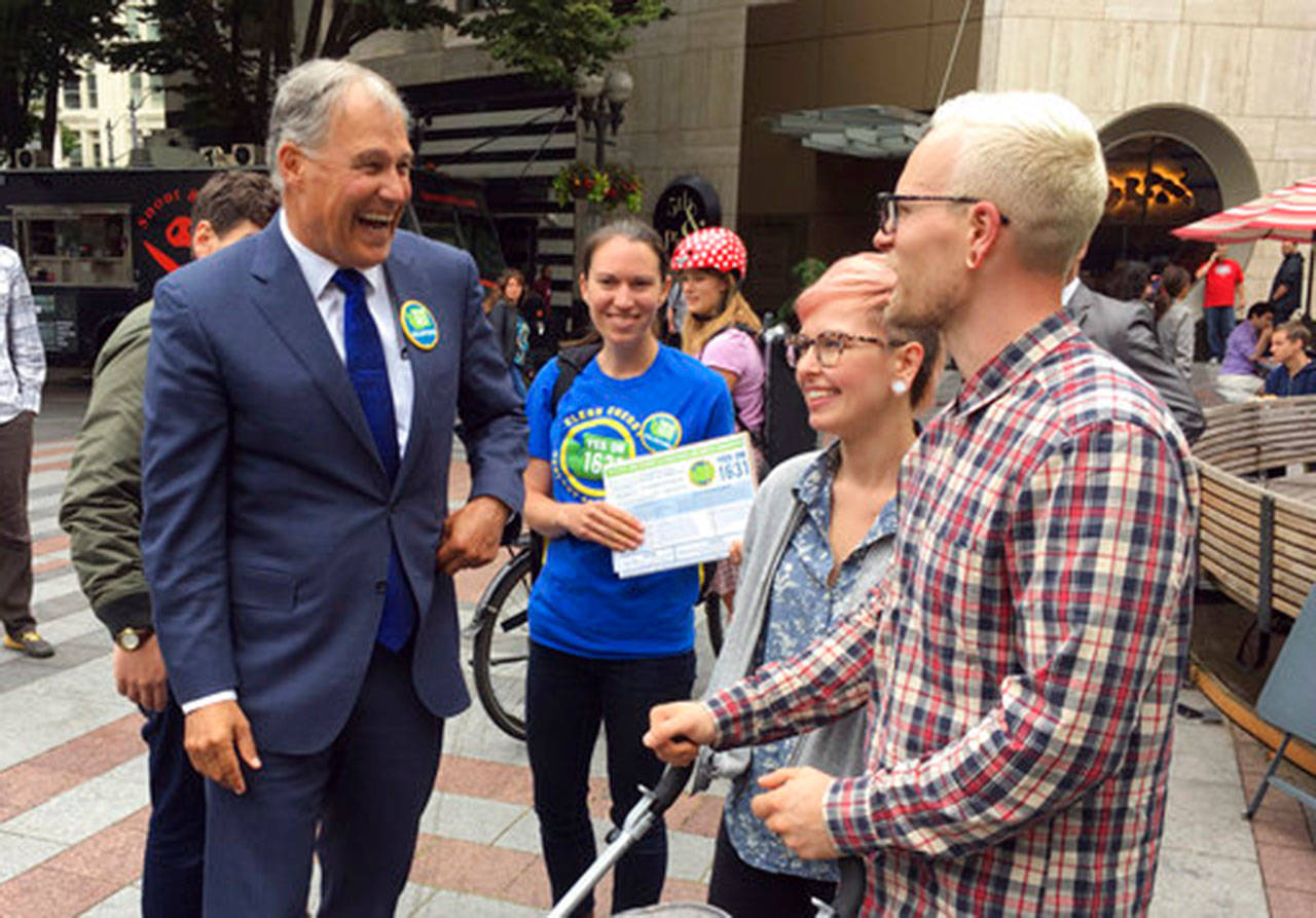 Gov. Jay Inslee speaks to people on June 28 in Seattle as he helps to gather signatures for a proposed initiative that would charge large industrial emitters a fee for their carbon emissions. (Phuong Le/The Associated Press)