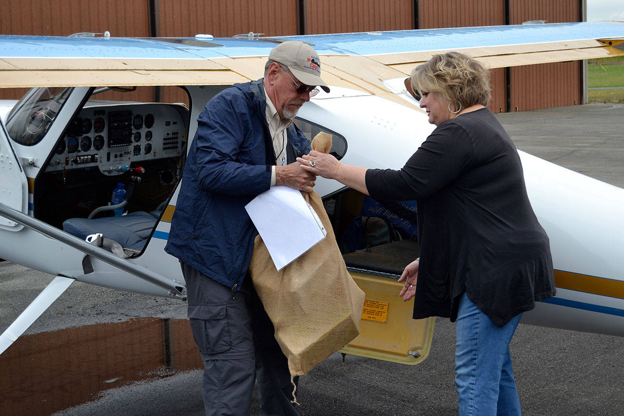 Ray Ballantyne, a volunteer with Disaster Aircraft Response Team (DART) hands a bag of food to Andra Smith, Sequim Food Bank executive director, at the Sequim Valley Airport on Saturday. (Matthew Nash/Olympic Peninsula News Group)