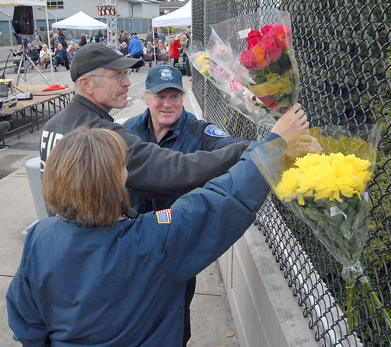 Port Angeles police volunteers Pam Ogier, left, and Darrel Reetz, right, along with Clallam County Fire District No. 2 Lt. Al Oman, center, place a bouquet of eight roses on suicide barriers on the Eighth Street bridge over Valley Creek in honor of the eight people who leapt to their deaths since 2009. The completion of fencing installation was celebrated during a community gathering and concert Wednesday evening in Port Angeles. (Keith Thorpe/Peninsula Daily News)