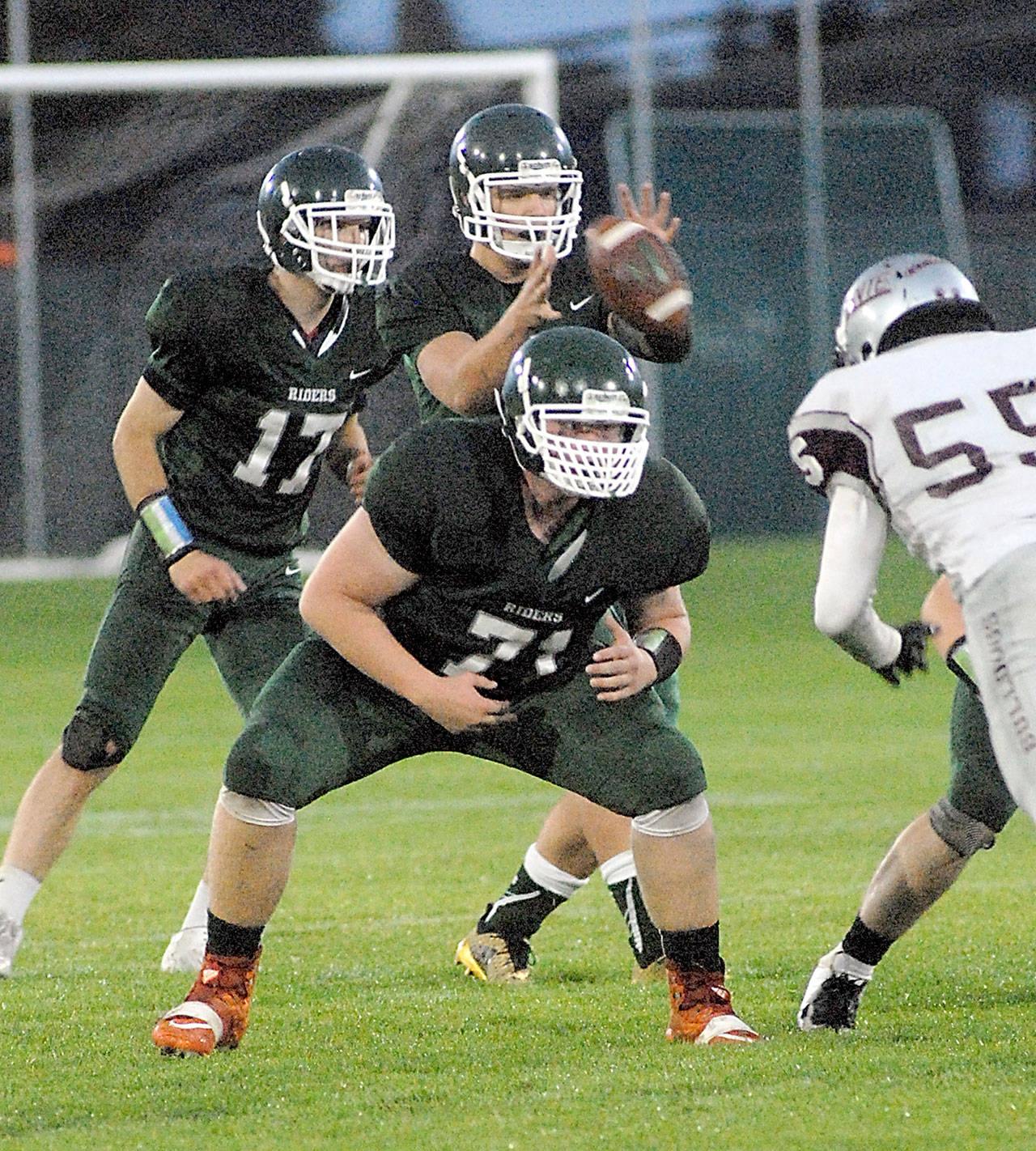 Keith Thorpe/Peninsula Daily News Port Angeles quarterback Brenden Roloson-Hines, back, receives the snap surrounded by teammates Garrett Edwards, left, and Cole Walsh as Montesano’s Kai Olson closes in during last Friday’s game at Port Angeles Civic Field.