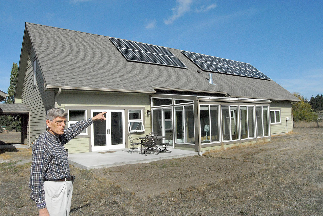 David Large points to a solar panel array and a glass-enclosed sun room that provide electricity and heat to his energy efficient home in rural Sequim. (Keith Thorpe/Peninsula Daily News)