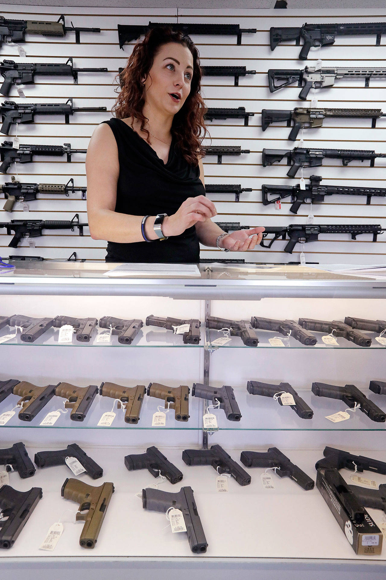 Lynnwood gun shop owner Tiffany Teasdale stands with pistols and semi-automatic rifles last Tuesday as she talks about a gun initiative on the upcoming ballot. (Elaine Thompson/The Associated Press)