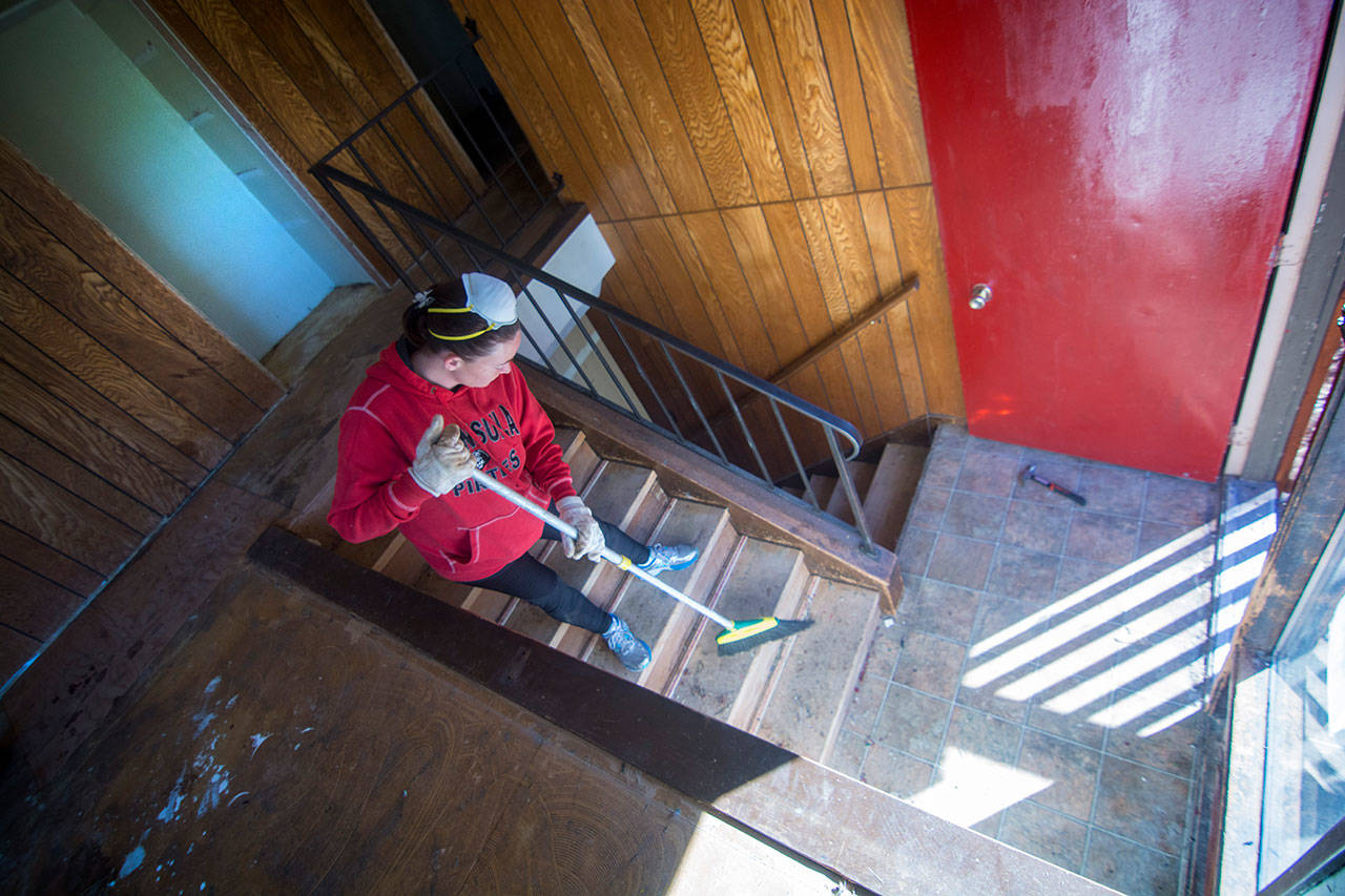 Brianna Kelly sweeps dust from stairs that were covered in carpet. She and other volunteers helped Saturday to renovate a property that is intended to become an Oxford House. (Jesse Major/Peninsula Daily News)