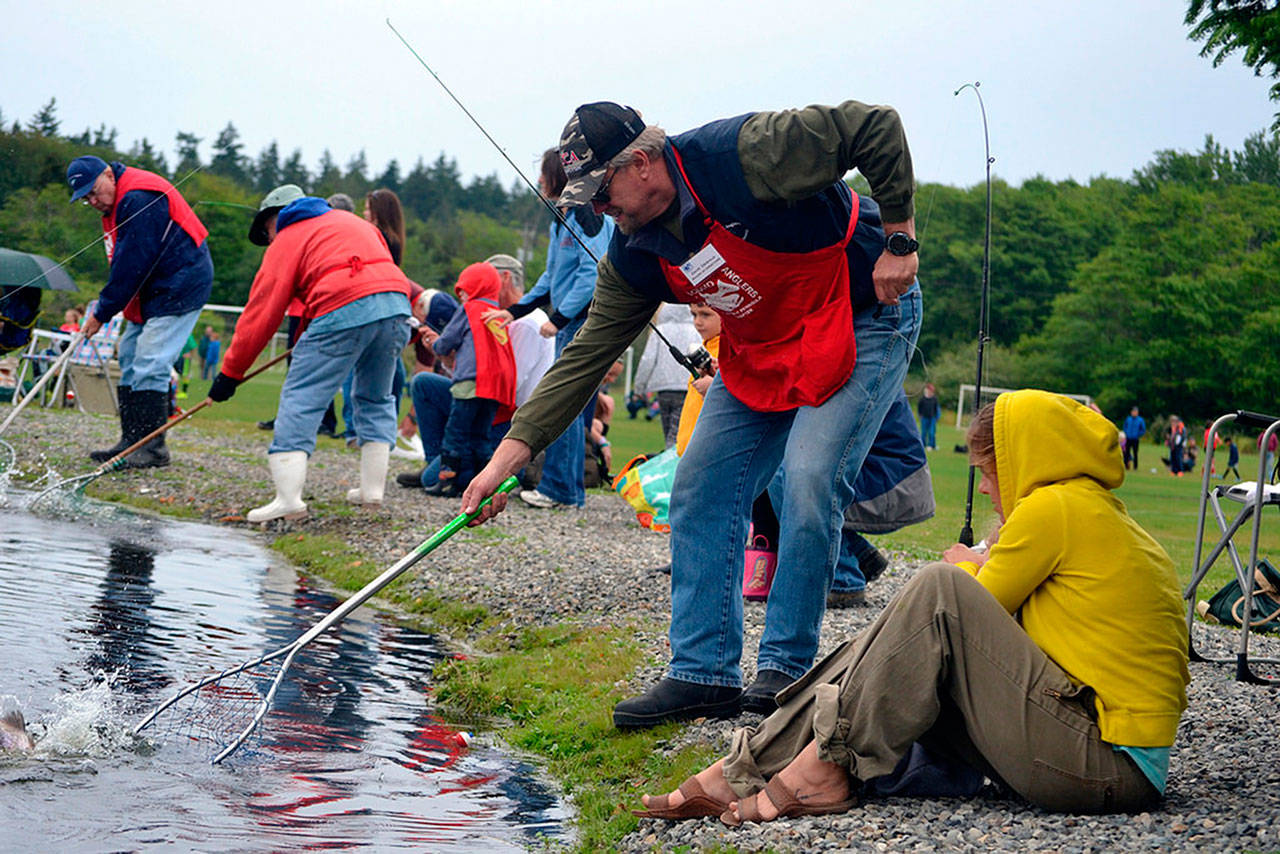 Jamie and Gibson Hill of Sequim pull in a fish while Dave Dewald tries to net it at Kids Fishing Day in 2016. The Puget Sound Anglers-North Olympic Chapter announced this week they have to cancel their 2018 event because of warm temperatures. (Matthew Nash/Olympic Peninsula News Group)