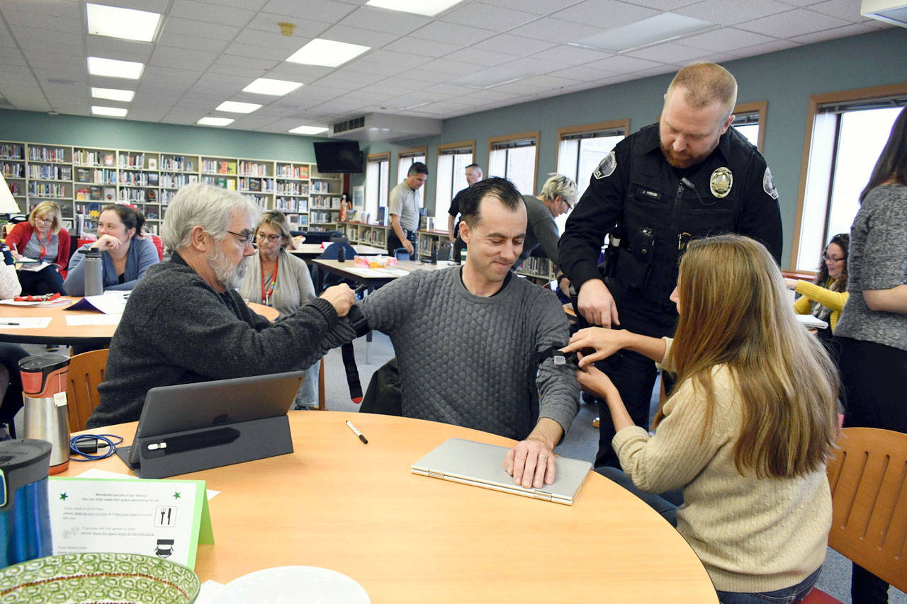 Port Townsend School Resource Officer Jeremy Vergin instructs social studies teacher Julianne Dow on how to apply a tourniquet to fellow social studies teacher Benjamin Dow. Media studies teacher Mark Welch works on Dow’s right arm. Members of Port Townsend High School’s staff learned how to “Stop the Bleed” during a professional development program recently. (Jeannie McMacken/Peninsula Daily News)