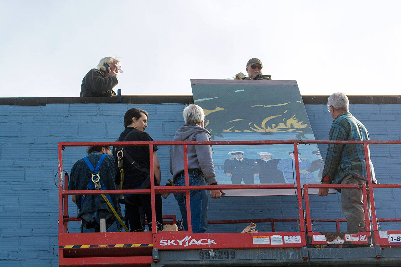 Bob Stokes, top left, watches as crews lower a panel of the Pacific Fleet mural to be installed on the west side of the former Station 51 Taphouse in Port Angeles on Monday afternoon. (Jesse Major/Peninsula Daily News)