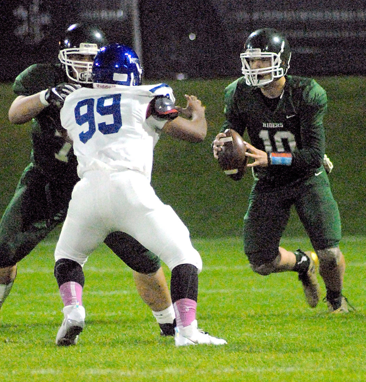 Keith Thorpe/Peninsula Daily News Port Angeles quarterback Brenden Roloson-Hines, right, looks downfield as teammate Darrell Duckett provides a block on North Mason’s Dom Dixon in the first quarter on Friday night at Port Angeles Civic Field.