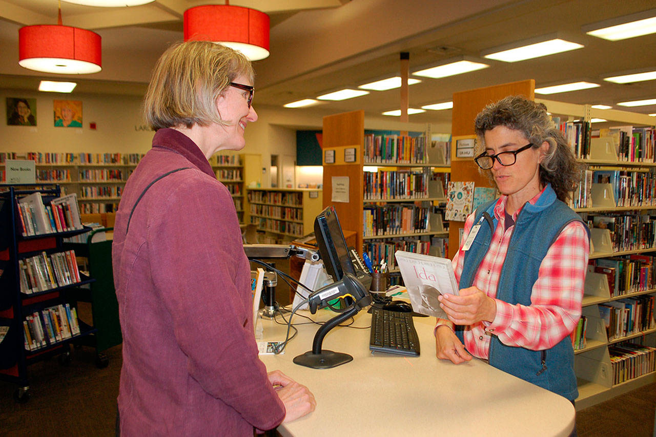 Sequim Library customer service specialist Mary Cote talks with Lindy MacLaine about a DVD at the Sequim Library. (Erin Hawkins/Olympic Peninsula News Group)