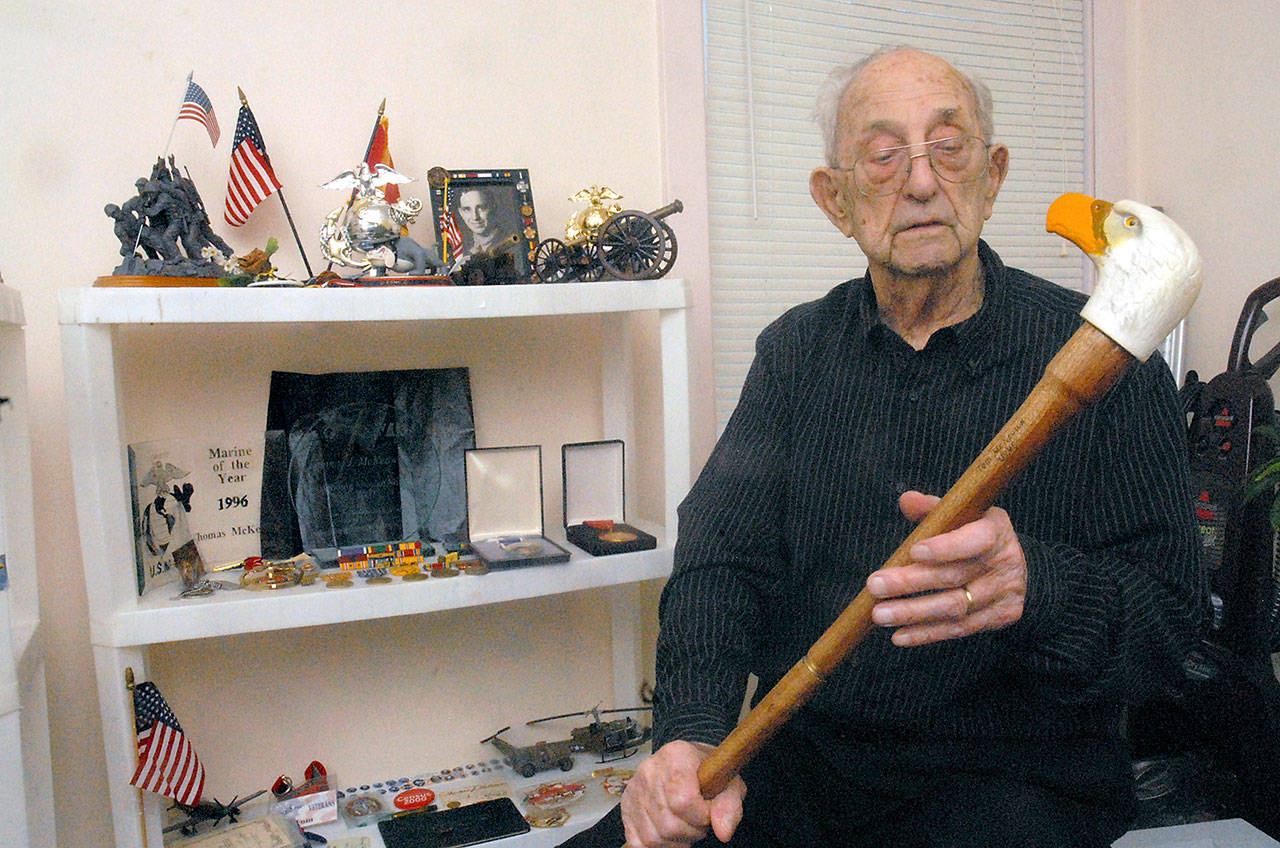U.S. Marine Corps veteran Tom McKeown Sr. of Port Angeles looks at a decorative walking stick next to a set of shelves filled with medals and other memoribilia relating to his service during World War II. (Keith Thorpe/Peninsula Daily News)