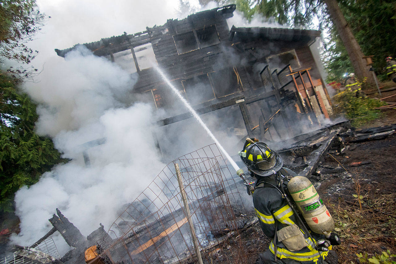 A firefighter puts water on Alice Derry’s house on Deer Park Road after it caught fire Tuesday afternoon. (Jesse Major/Peninsula Daily News)