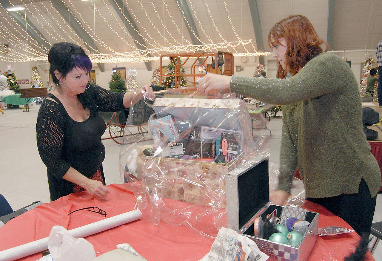 Tree decorators Trish Wray, left, and Brittney Vincent put the finishing touches on a premium package to accompany a Christmas tree sponsored by Swain’s General Store during final preparations Wednesday for this weekend’s Festival of Trees at Vern Burton Community Center in Port Angeles. (Keith Thorpe/Peninsula Daily News)