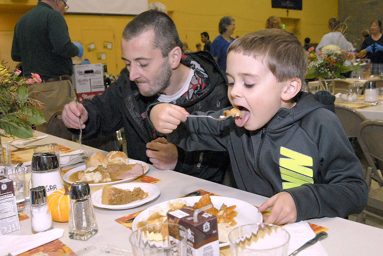 Five-year-old Tyler Dalgardno of Port Angeles takes a bite of his meal with his uncle, Stephen McBride of Port Angeles, left, during Thursday’s community Thanksgiving dinner in the gym of Queen of Angels Catholic Church in Port Angeles. (Keith Thorpe/Peninsula Daily News)