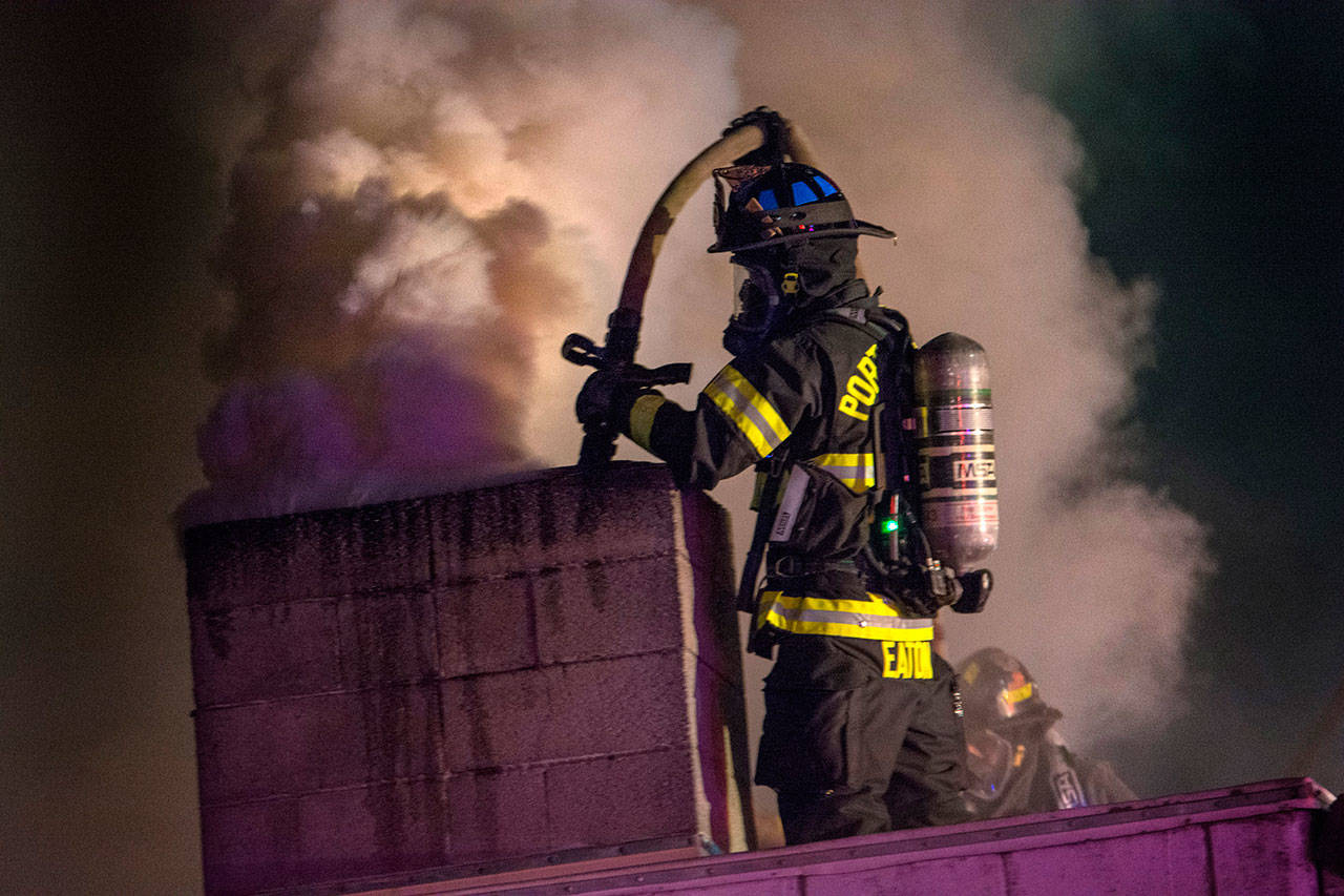 Firefighter Doug Eaton of the Port Angeles Fire Department sprays down the chimney of Sunrise Meats late Saturday night. (Jesse Major/Peninsula Daily News)