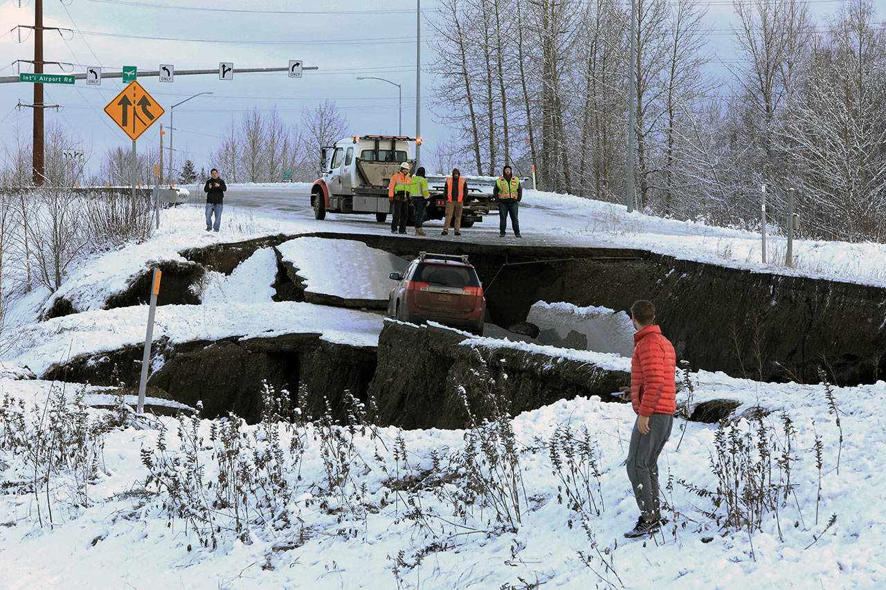 Highway workers and spectators look at a car stuck on a section of an off-ramp that collapsed during an earthquake Friday morning in Anchorage, Alaska. The driver was not injured attempting to exit Minnesota Drive at International Airport Road. (Dan Joling/The Associated Press)