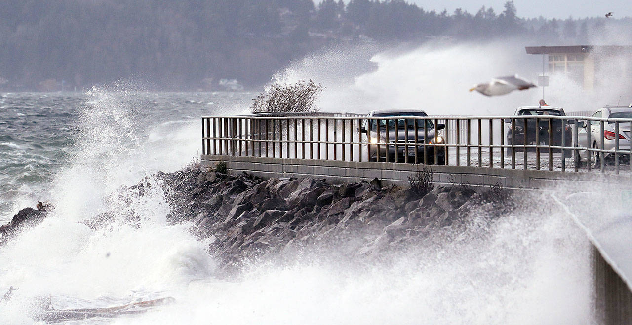 Waves crash against a seawall at high tide as cars maneuver past during a windstorm Thursday in Seattle. (Elaine Thompson/The Associated Press)