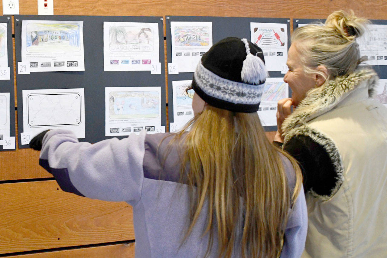 Volunteer Sandra Burkette, right, discusses children’s artwork for a license plate design Saturday with a voter at a display of 48 entries at the Cotton Building in Port Townsend. The Fariborz Youssefirad Memorial Health Scholarship plans to submit the winning design chosen by the public to the Legislature next year to be approved for the special issue. The focus of the plate and program is education for the prevention of Type 2 diabetes in children. (Jeannie McMacken/Peninsula Daily News)