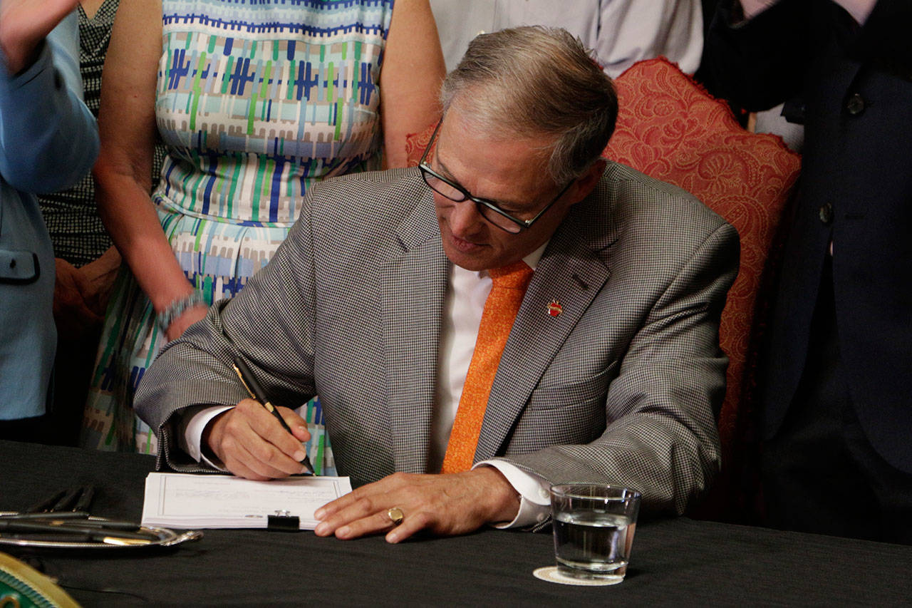 In this July 5, 2017 file photo, Washington Gov. Jay Inslee signs into law a measure that makes Washington one of a hand full of states that guarantee paid family leave in Olympia, Wash. Employers and employees in Washington state will start paying into a new paid family leave program next week, and benefits from the program will begin in 2020. (AP Photo/Rachel La Corte, file)