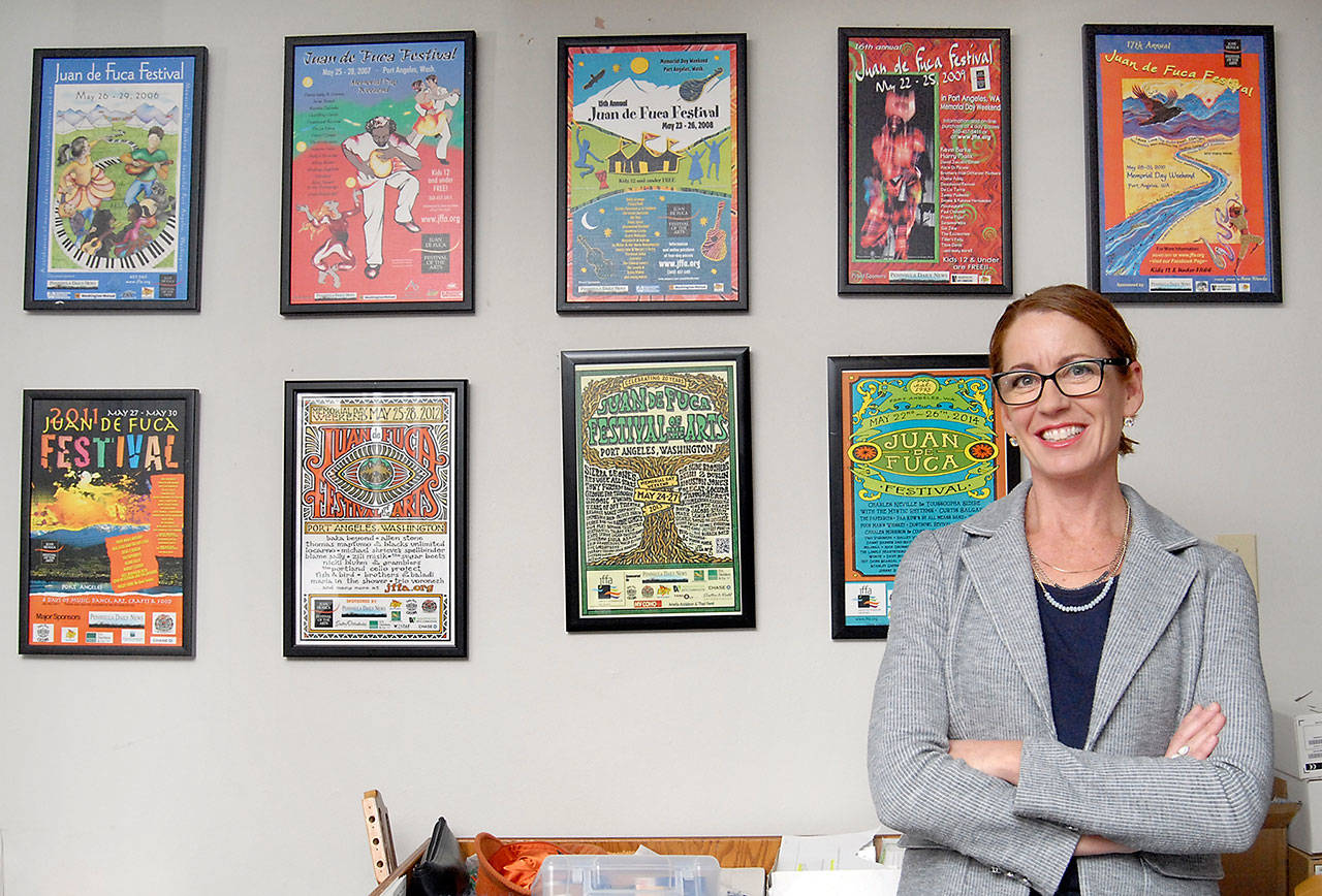 New Juan de Fuca Foundation for the Arts Executive Director Kayla Oakes stands before a display of previous festival posters in the organization’s Port Angeles office. (Keith Thorpe/Peninsula Daily News)