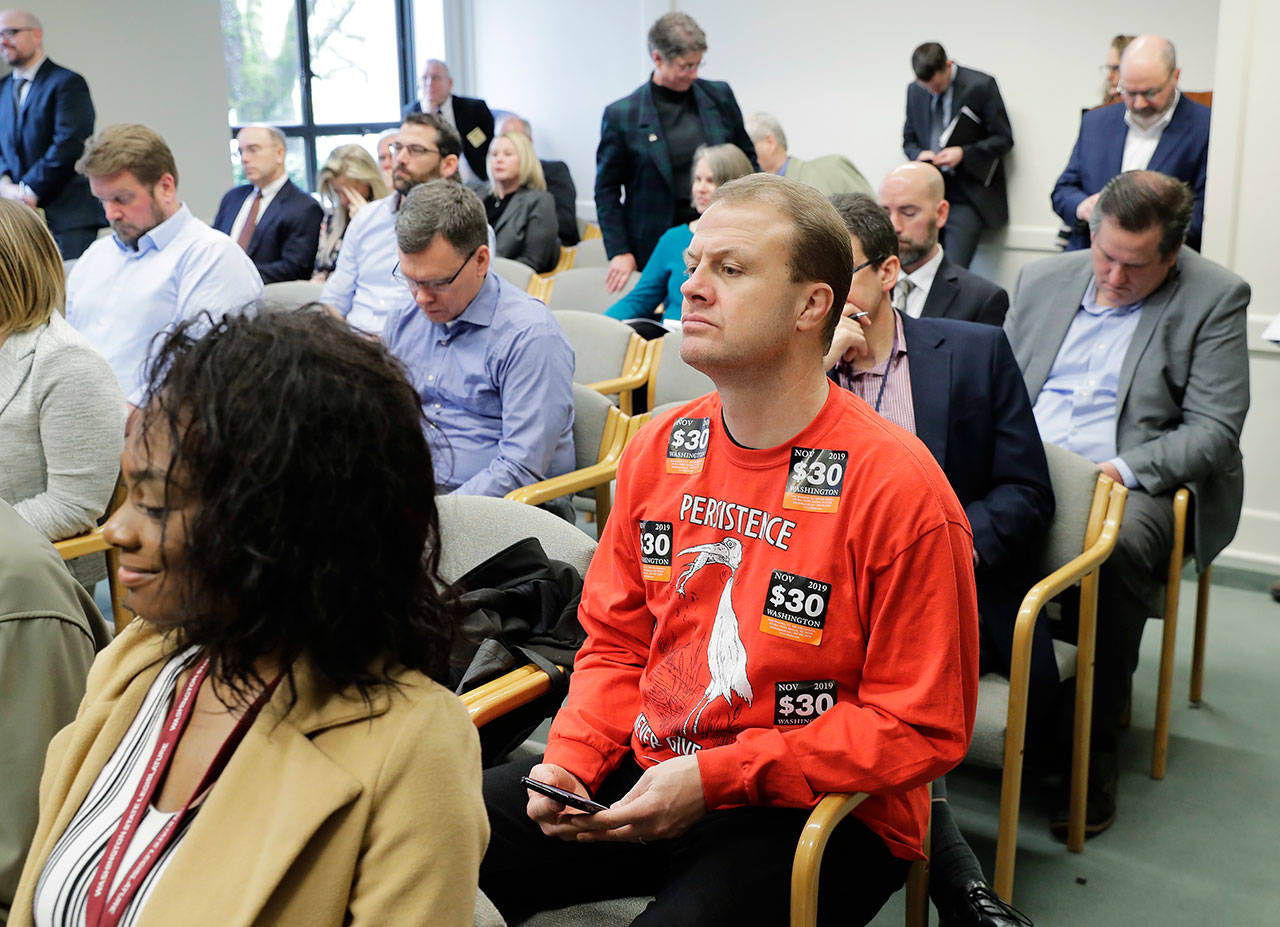 Anti-tax activist Tim Eyman, right, wears a sweatshirt with stickers from his I-976 $30 car tabs initiative on it as he attends the Associated Press Legislative Preview on Thursday at the Capitol in Olympia. (Ted S. Warren/The Associated Press)