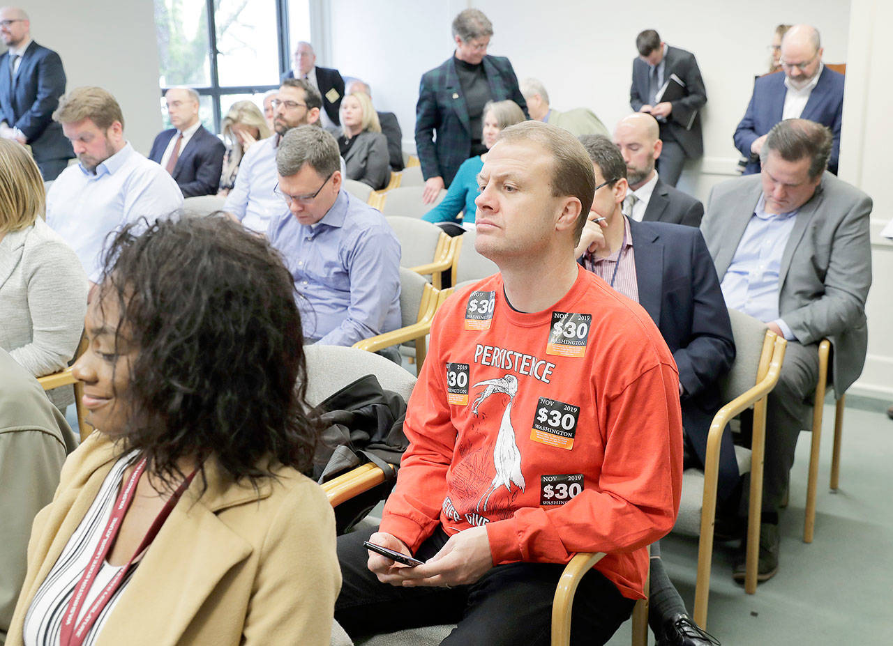 Anti-tax activist Tim Eyman, right, wears a sweatshirt with stickers from his I-976 $30 car tabs initiative on it as he attends the Associated Press Legislative Preview at the Capitol in Olympia on Jan. 10. (Ted S. Warren/The Associated Press)