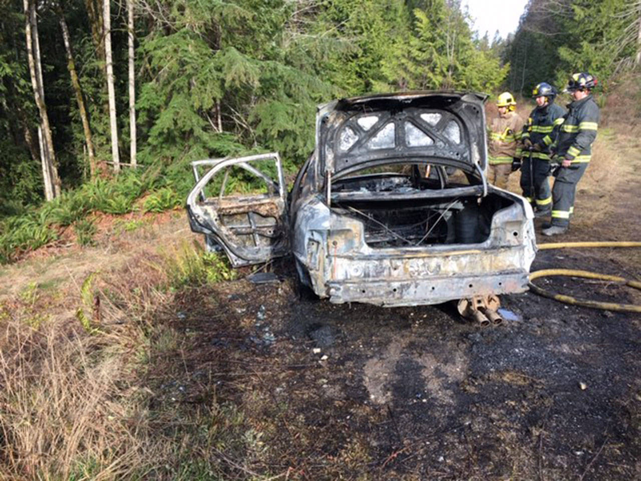 Firefighters from Clallam County Fire District 2 look over a vehicle that was fully engulfed in flames off U.S. Highway 101 near Milepost 241 on Monday. (Clallam County Fire District 2)