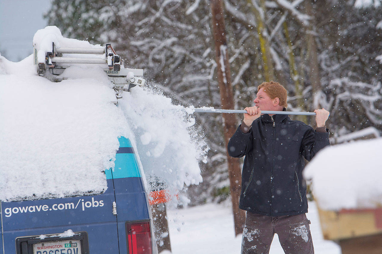 Ryan Wetterlund clears snow from his work vehicle as snow continued to fall Monday morning. (Jesse Major/Peninsula Daily News)