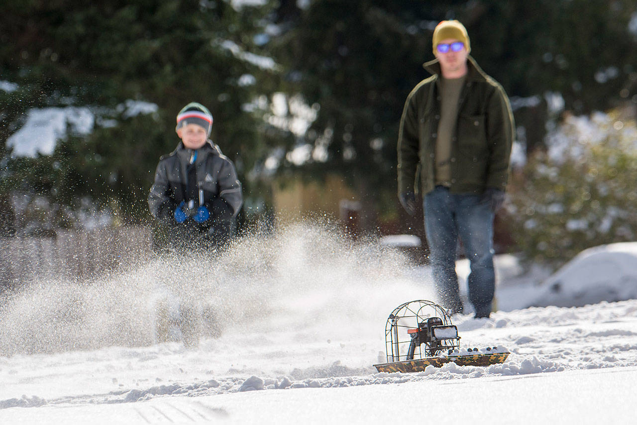 Brian Winters watches on as his 9-year-old son Cole uses a remote controlled air boat at the snow-covered field at Stevens Middle School in Port Angeles on Sunday. (Jesse Major/Peninsula Daily News)