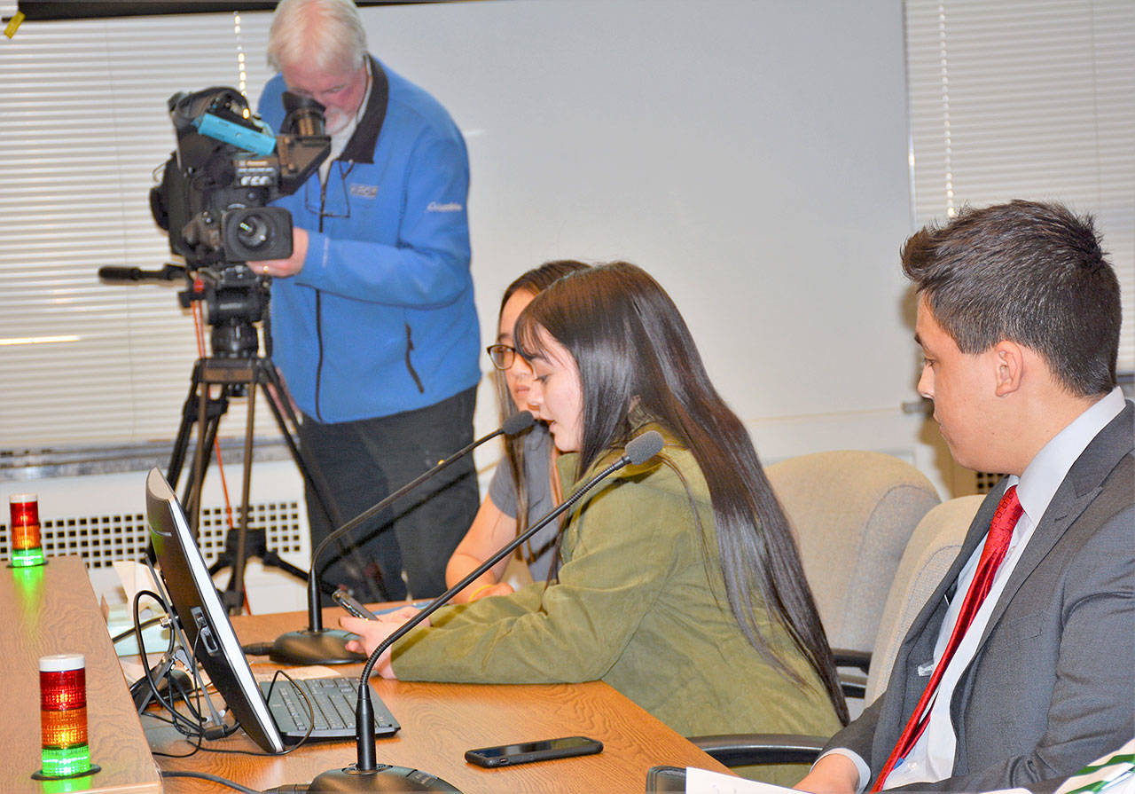 The PASD team prepares to deliver testimony with only 60 seconds allowed for each speaker. The lights on the witness table indicate green for “go,” yellow for “warning,” then red for “stop.” From left are Abby Sanders, Hailey Robinson, speaking into the microphone, and Andrew Pena. (Patsene Dashiell/Port Angeles School District)