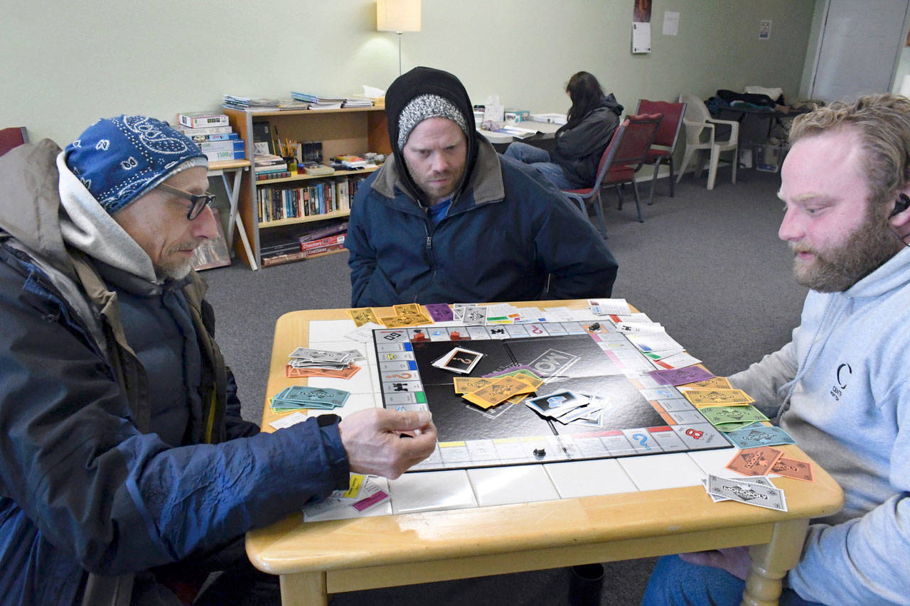 The newly opened Warming Center on East Sims Way in Port Townsend has become a welcoming place for those who are looking for a safe, comfortable place to be after the Winter Shelter closes at 8 a.m. From left, Lawrence Alan, Steven Riggs and Ben Casserd had a friendly Monopoly game going Tuesday. (Jeannie McMacken/Peninsula Daily News)