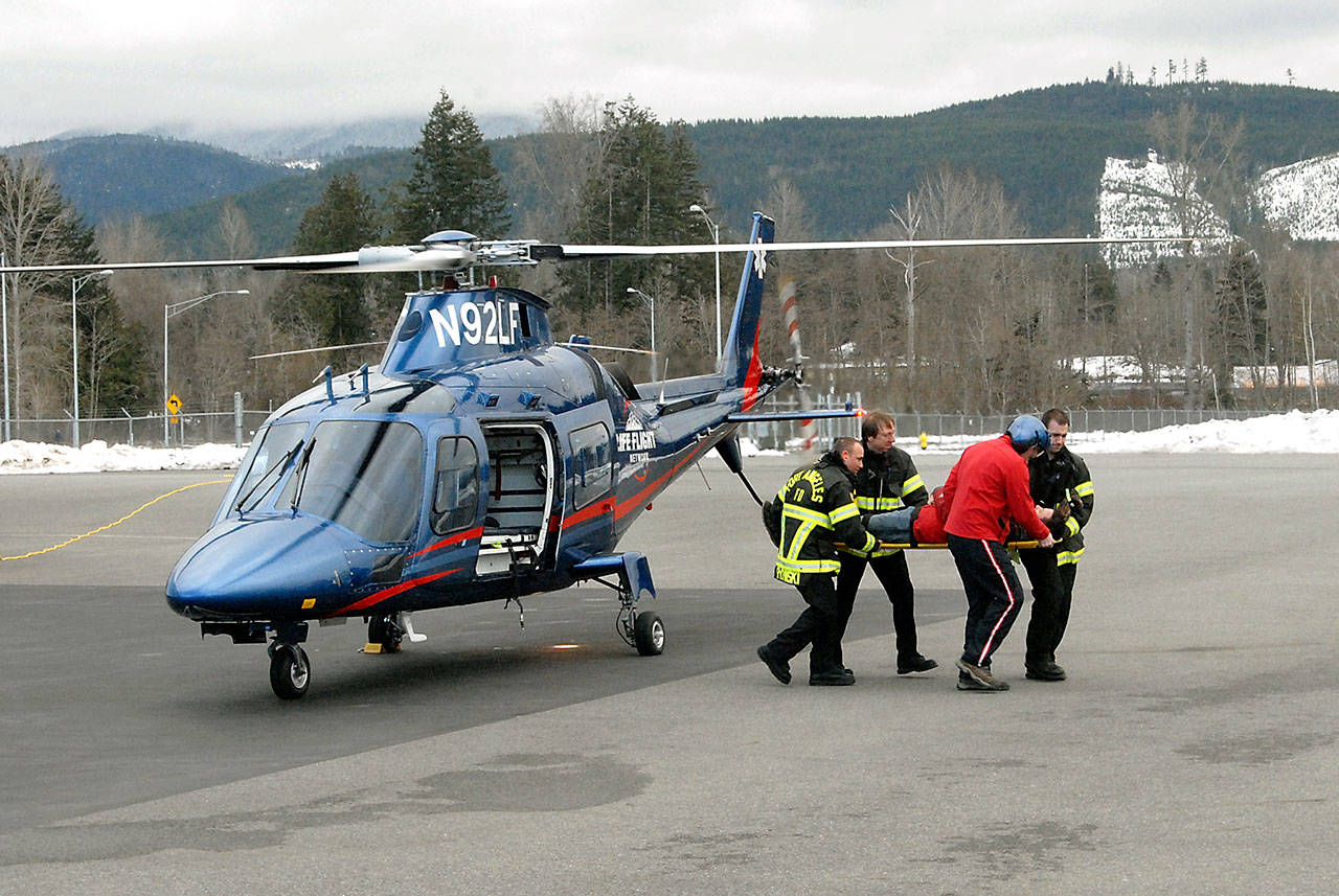 Port Angeles firefighters, from left, Dayvid Rypinski, Capt. Terry Reid and George Kourdahi, along with Life Flight Network’s David Salisbury, carry Life Flight mechanic and mock victim Steven Varlay during a familiarization training exercise with a AW109 medical helicopter at William R. Fairchild International Airport. (Keith Thorpe/Peninsula Daily News)